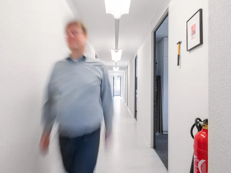 EIn Entwickler eilt zur Hilfe; heller Gang mit Feuerlöscher, sowie einem Hammer und einem Bild an der rechten Wand